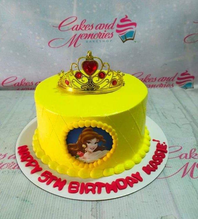 Yellow Belle princess themed birthday cake with a gold tiara and a printed character image on the side.