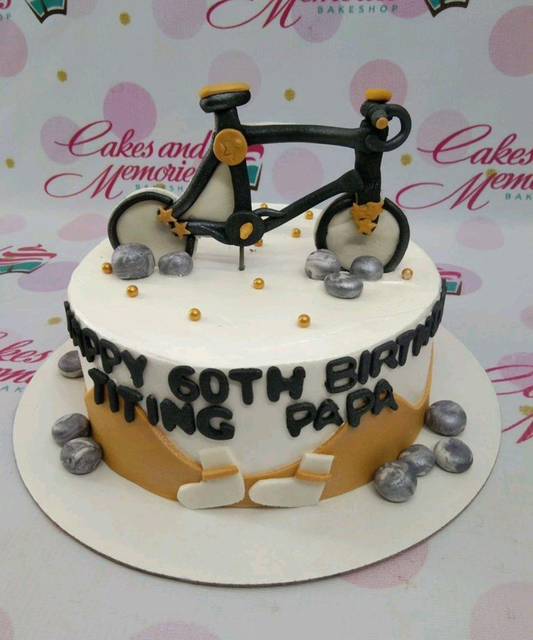 White 60th birthday cake for Papa featuring a detailed black and gold bicycle topper, silver fondant rocks, and gold dragees.