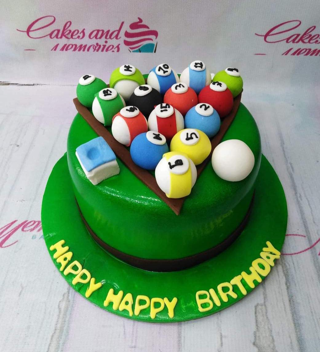 Green billiard pool table cake with fondant billiard balls, a cue ball, and a blue chalk cube on a green base board.