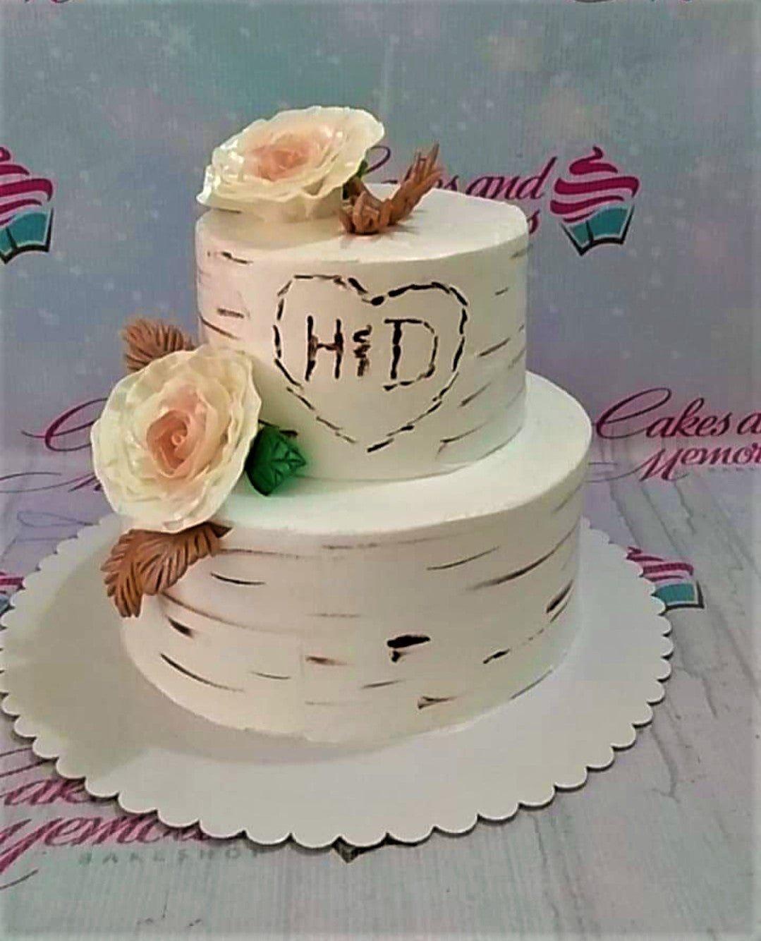 Two-tier white birch tree themed cake with edible pink roses and carved initials H and D inside a heart.