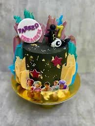 Black and gold themed cake with colorful icing strokes, gold leaf accents, and character printouts on a gold base.