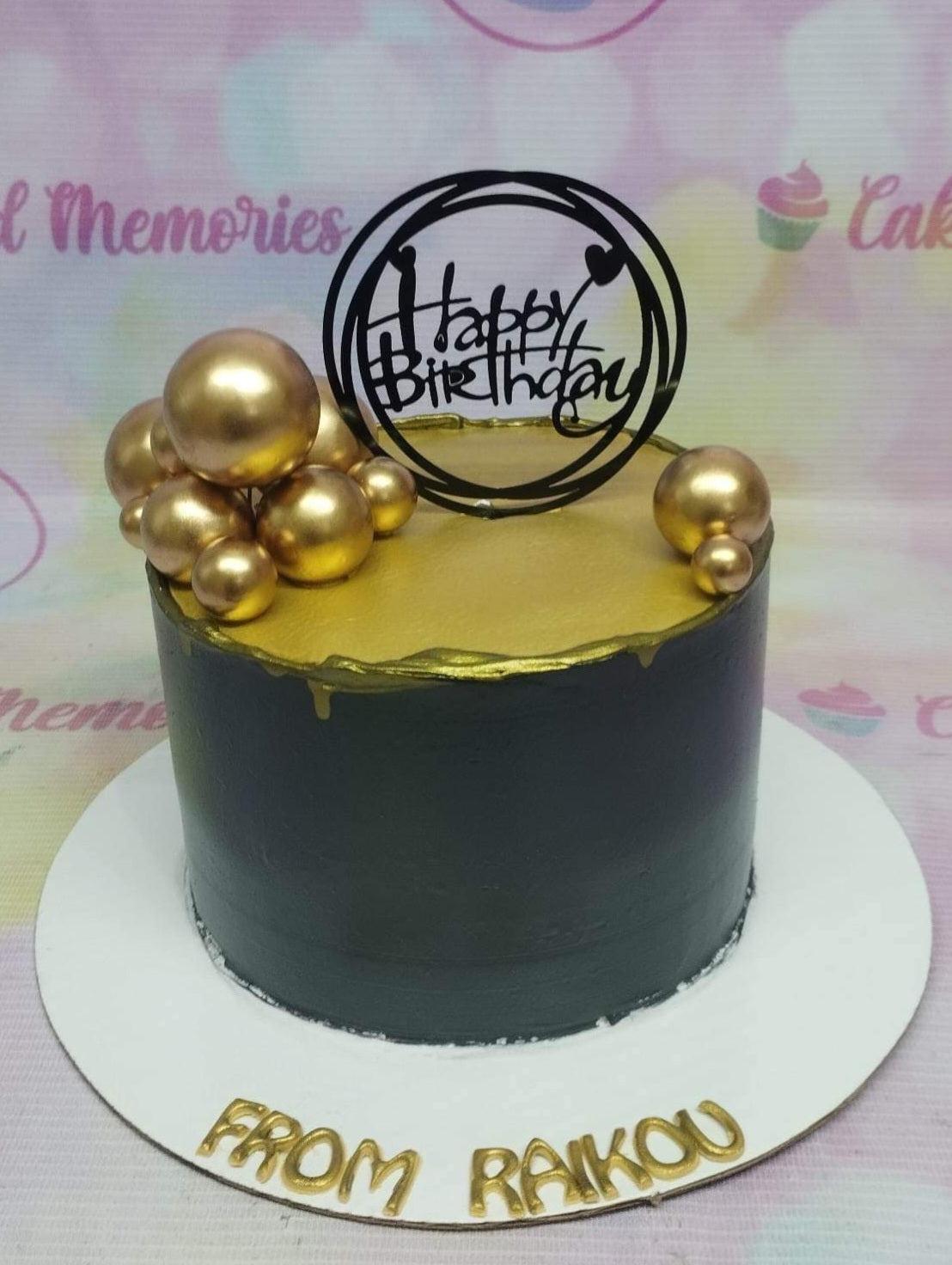 Elegant black and gold birthday cake with metallic gold spheres and a black Happy Birthday topper.