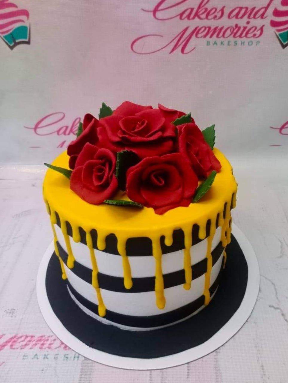 Single tier cake with black and white horizontal stripes, yellow drip, and a cluster of red fondant roses on top.