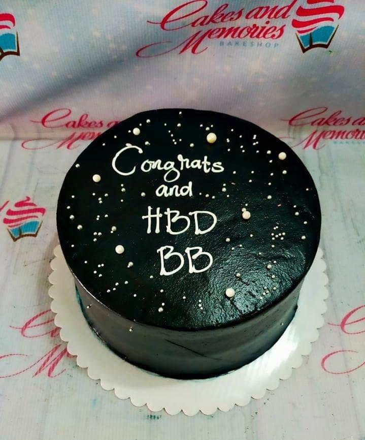 Black minimalist birthday cake with white piped icing message and silver and white pearl sprinkles.