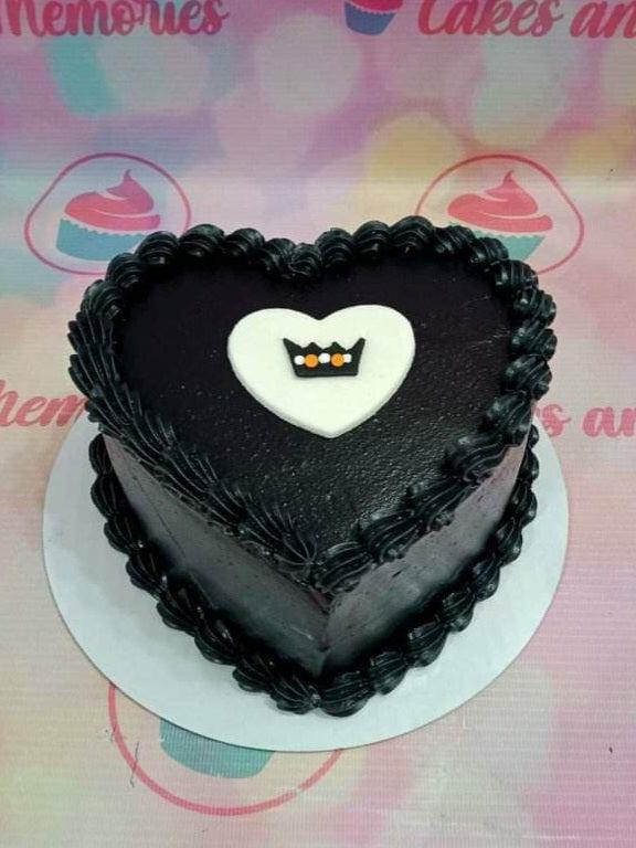 Heart-shaped black minimalist cake with black icing rosettes and a white heart topper with a small crown design.