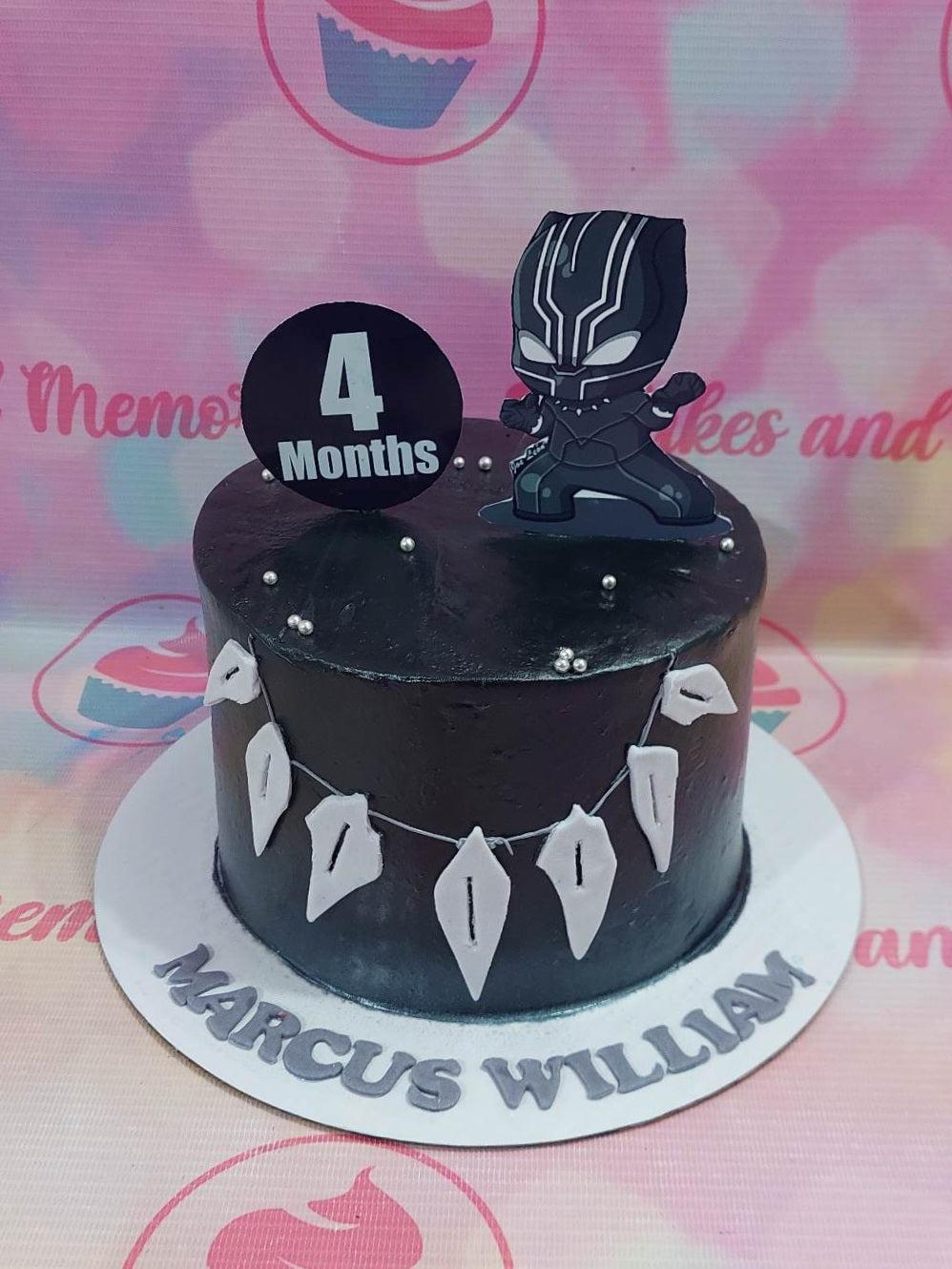 Black Panther themed birthday cake with black icing, silver dragees, white fondant necklace details, and a Black Panther character topper.