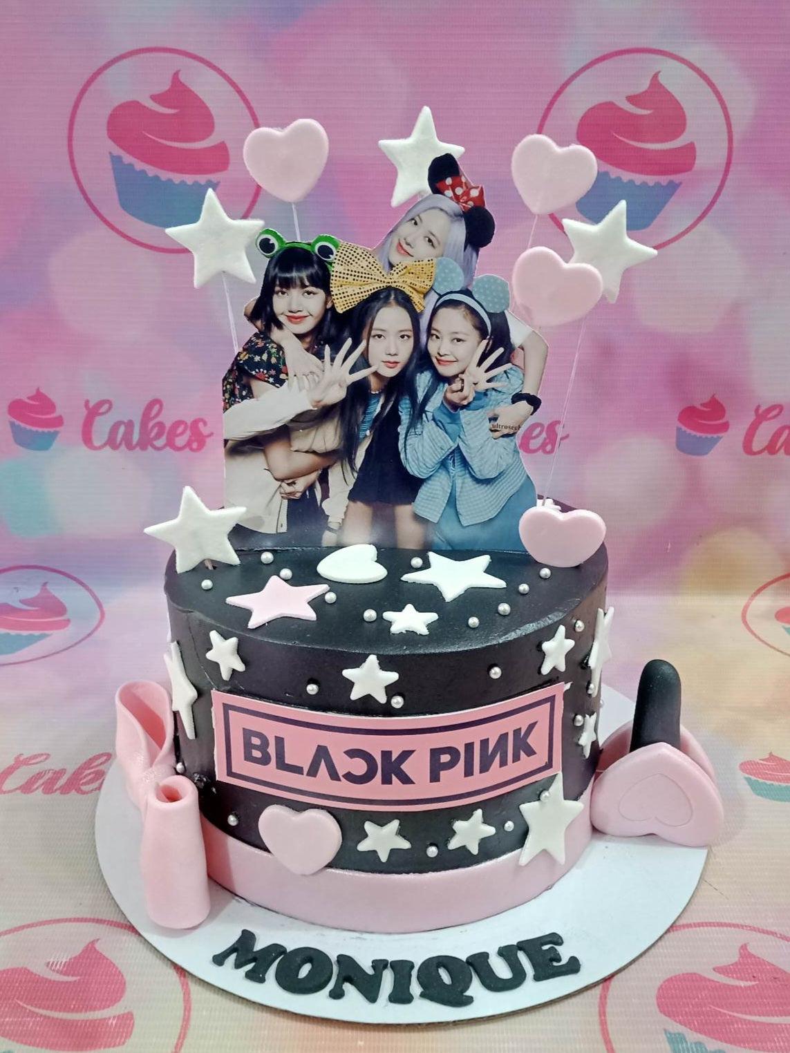 Black and pink Blackpink themed cake with character printouts, fondant stars, hearts, and a lipstick topper.