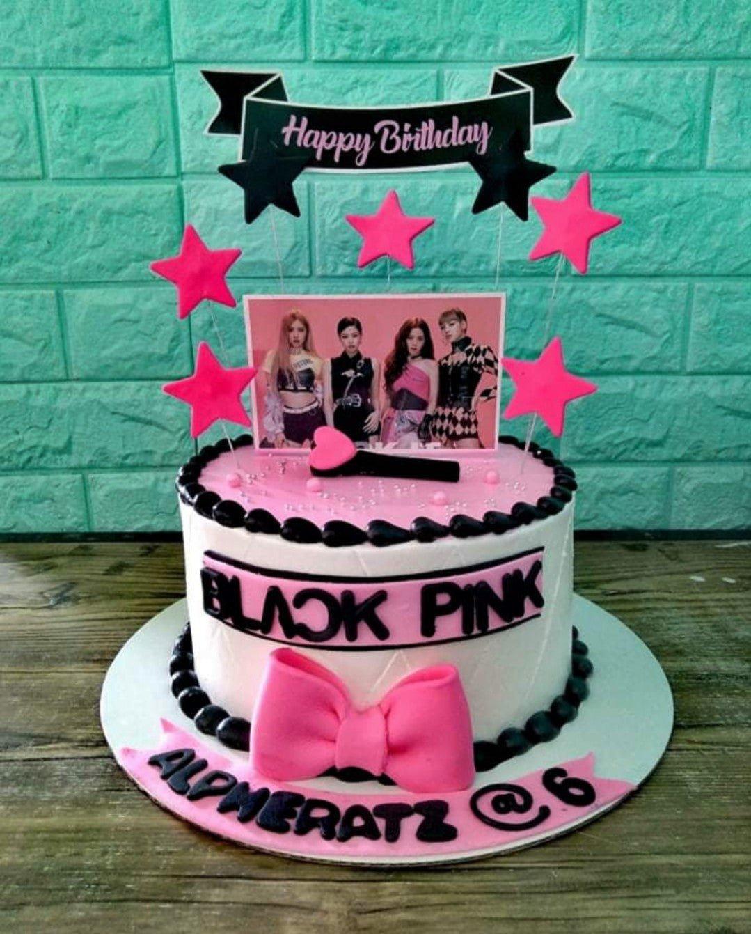 Blackpink themed birthday cake with pink and white icing, black borders, a large pink bow, and printed character toppers.
