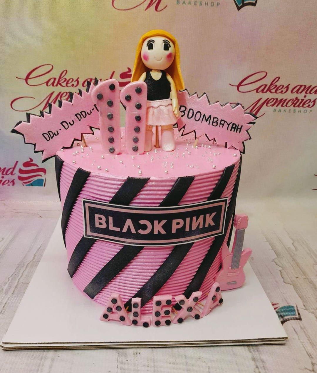 Pink Blackpink themed cake with diagonal black stripes, a fondant girl figure, and pink guitar topper.