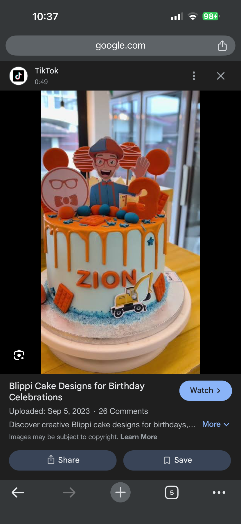 A light blue 1 tier cake featuring a Blippi character, the name 'ZION', blue fondant balls, and orange chocolate bars.