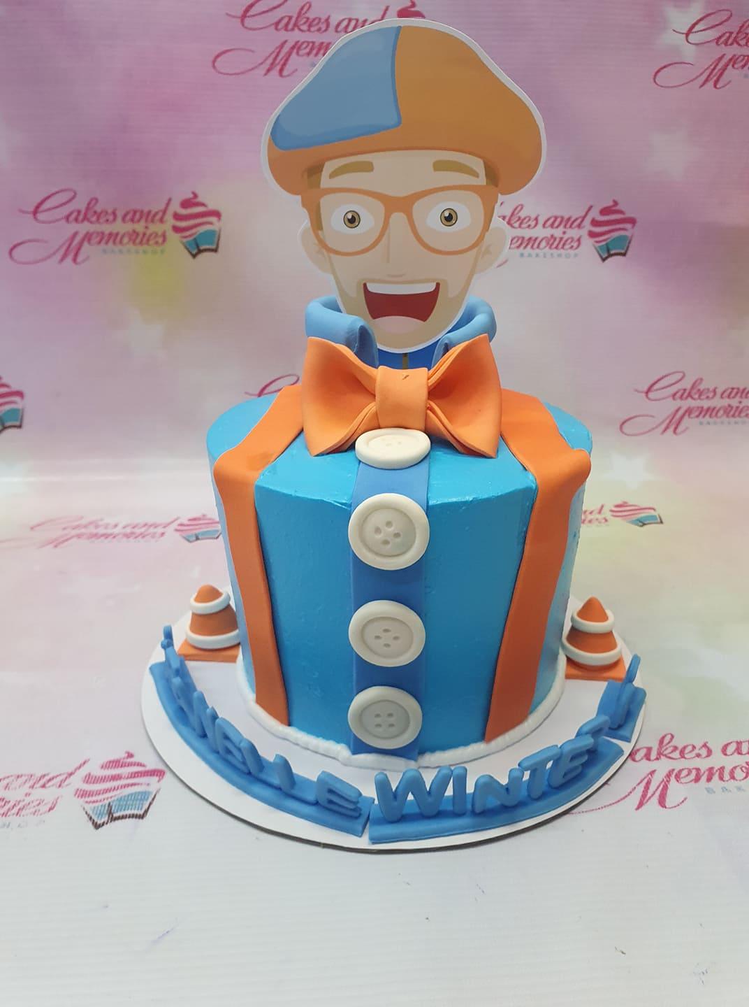 Blippi themed blue and orange tuxedo cake with a large character printout topper and fondant buttons.