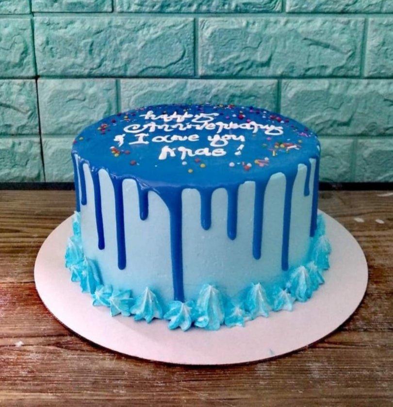 Light blue anniversary cake with dark blue drip, rainbow sprinkles, and white icing message.