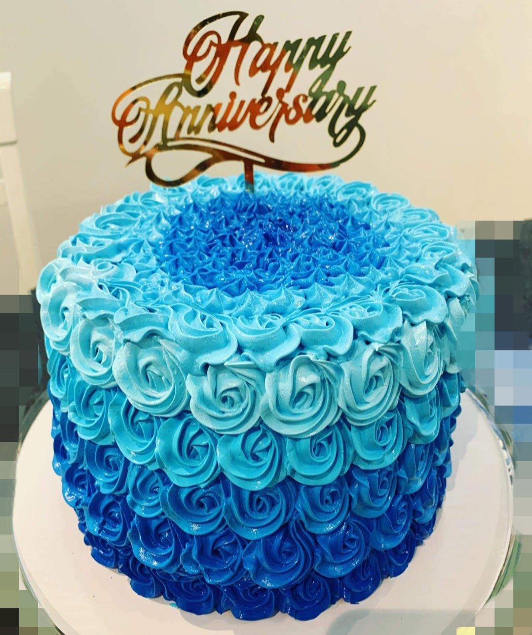 Single tier cake covered in blue ombre icing rosettes with a gold Happy Anniversary topper.