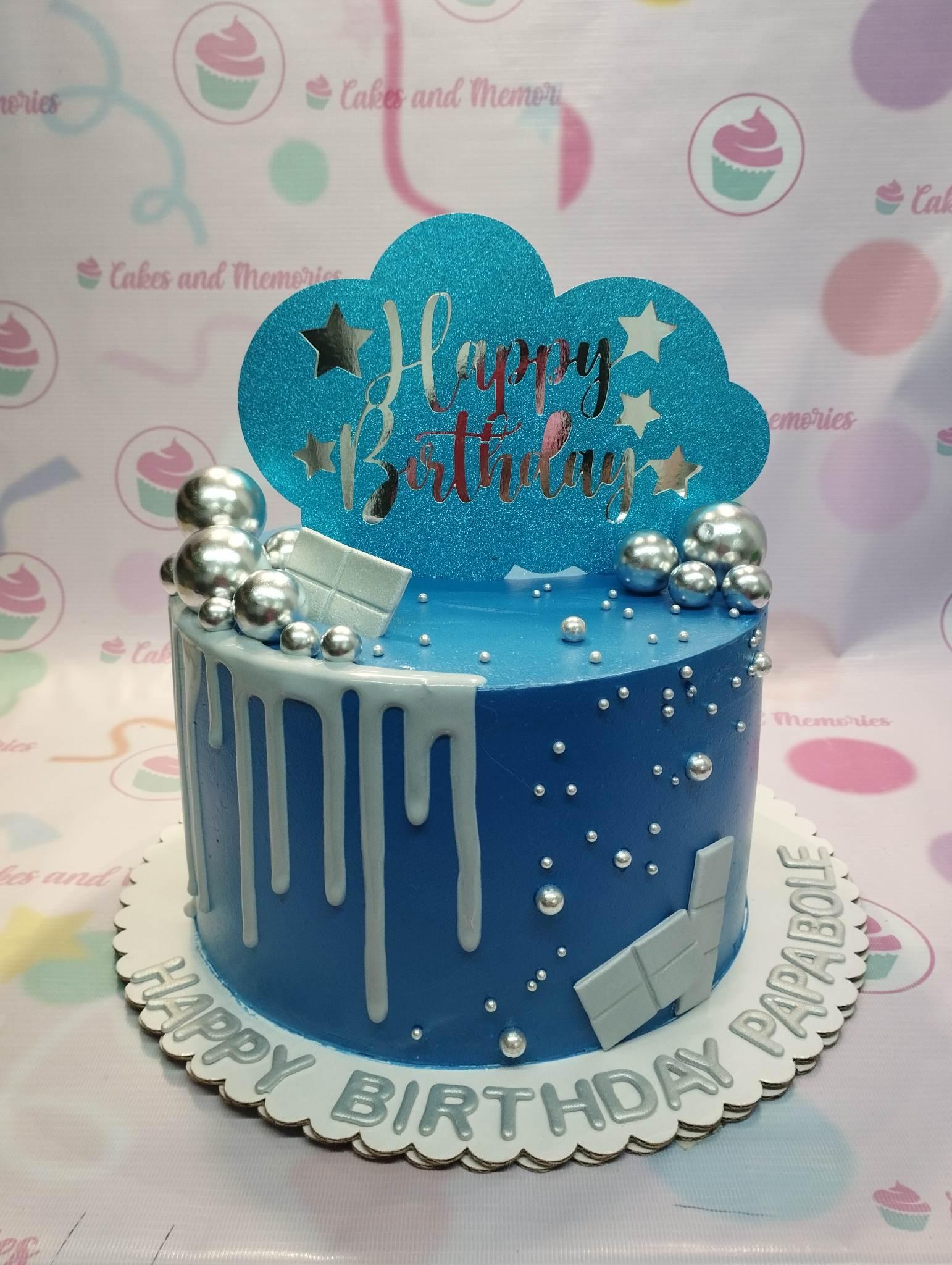 Blue birthday cake with silver drip, silver spheres, and a large blue glittery cloud topper with silver stars.