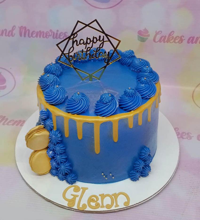 Blue birthday cake with gold drip, gold macarons, and a gold geometric Happy Birthday topper.
