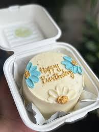 White bento cake with blue and white piped icing flowers and a gold Happy Birthday message