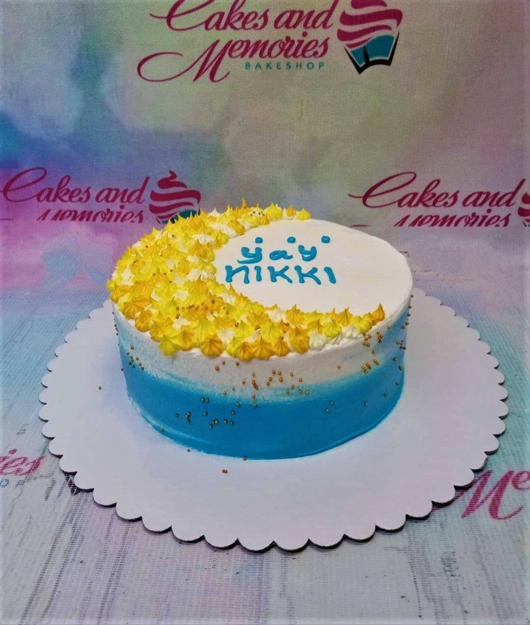 Single tier blue and white gradient cake with yellow icing rosettes and gold sprinkles