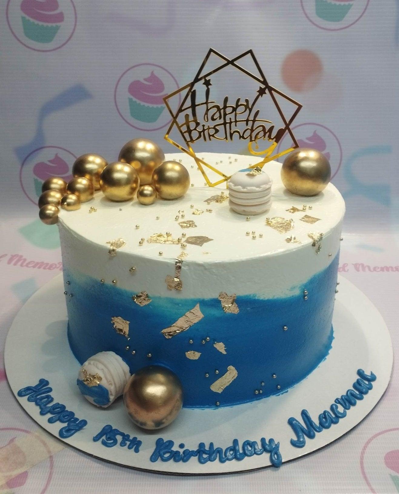 Blue and white gradient birthday cake with gold spheres, macarons, and a gold Happy Birthday topper.