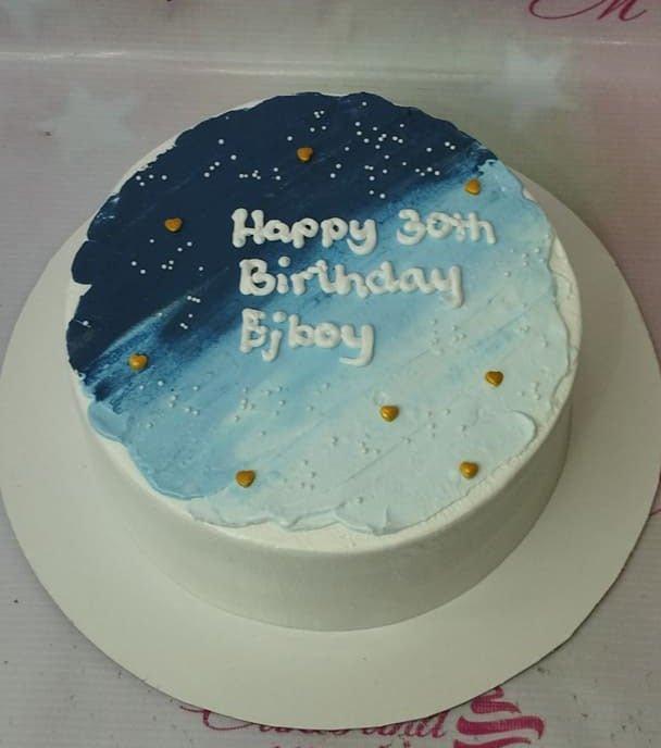 Minimalist blue and white birthday cake with a night sky design, gold hearts, and white piped icing message.