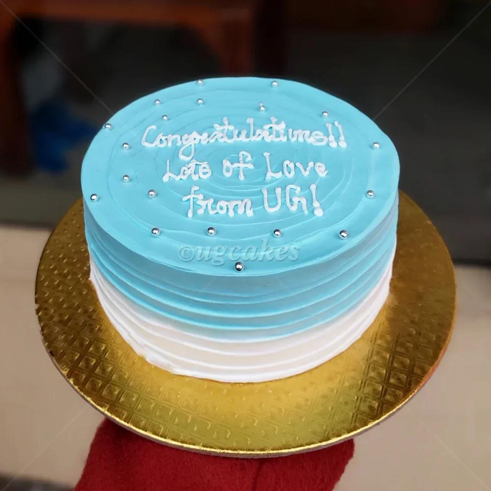 Light blue and white ombre minimalist cake with silver dragees and white icing message on a gold board.