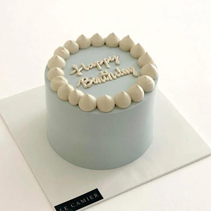 Minimalist light blue birthday cake with beige icing dollops and piped Happy Birthday message