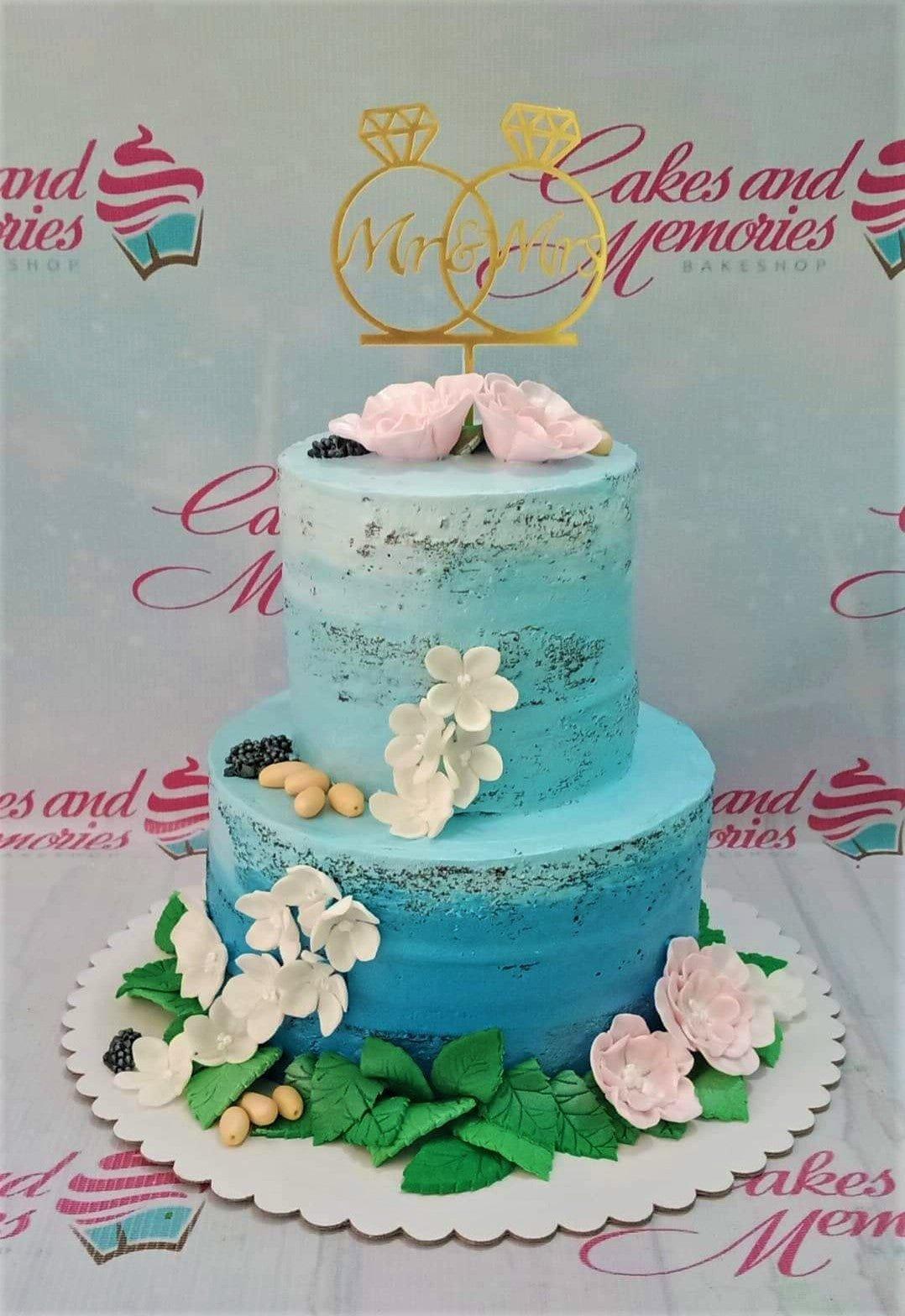 Two-tier blue ombre wedding cake with pink and white gumpaste flowers and a gold Mr & Mrs ring topper.