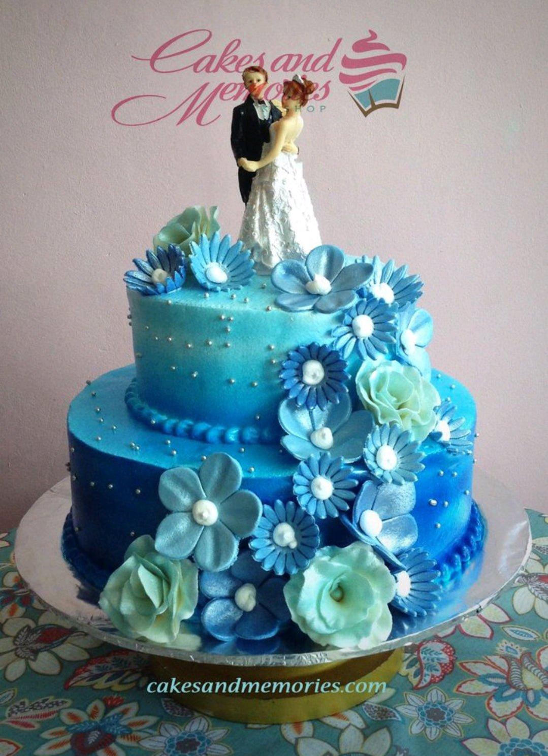 Two-tier blue ombre wedding cake decorated with blue and light green gumpaste flowers and a bride and groom topper.