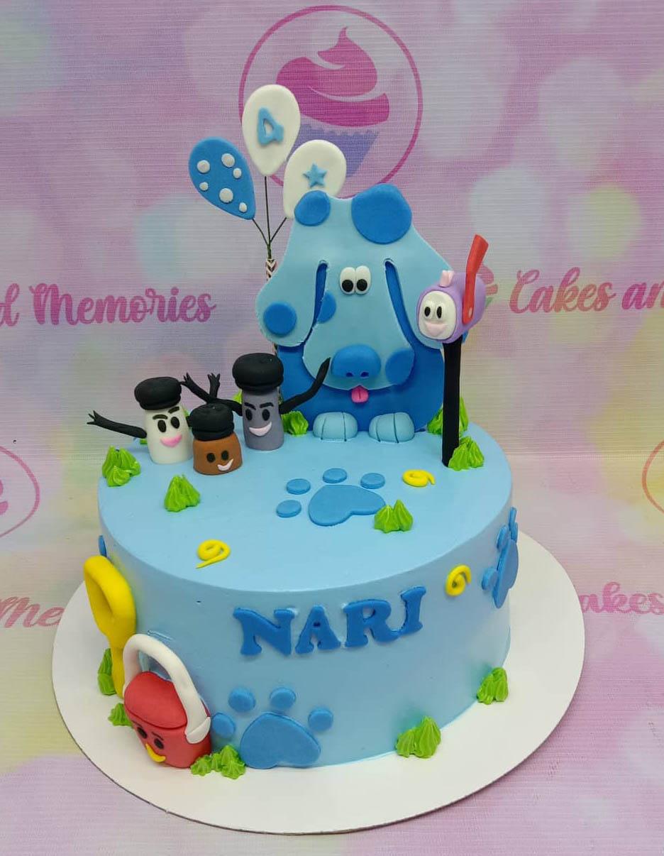 Light blue Blue's Clues themed birthday cake with fondant characters, paw prints, and a mailbox topper.