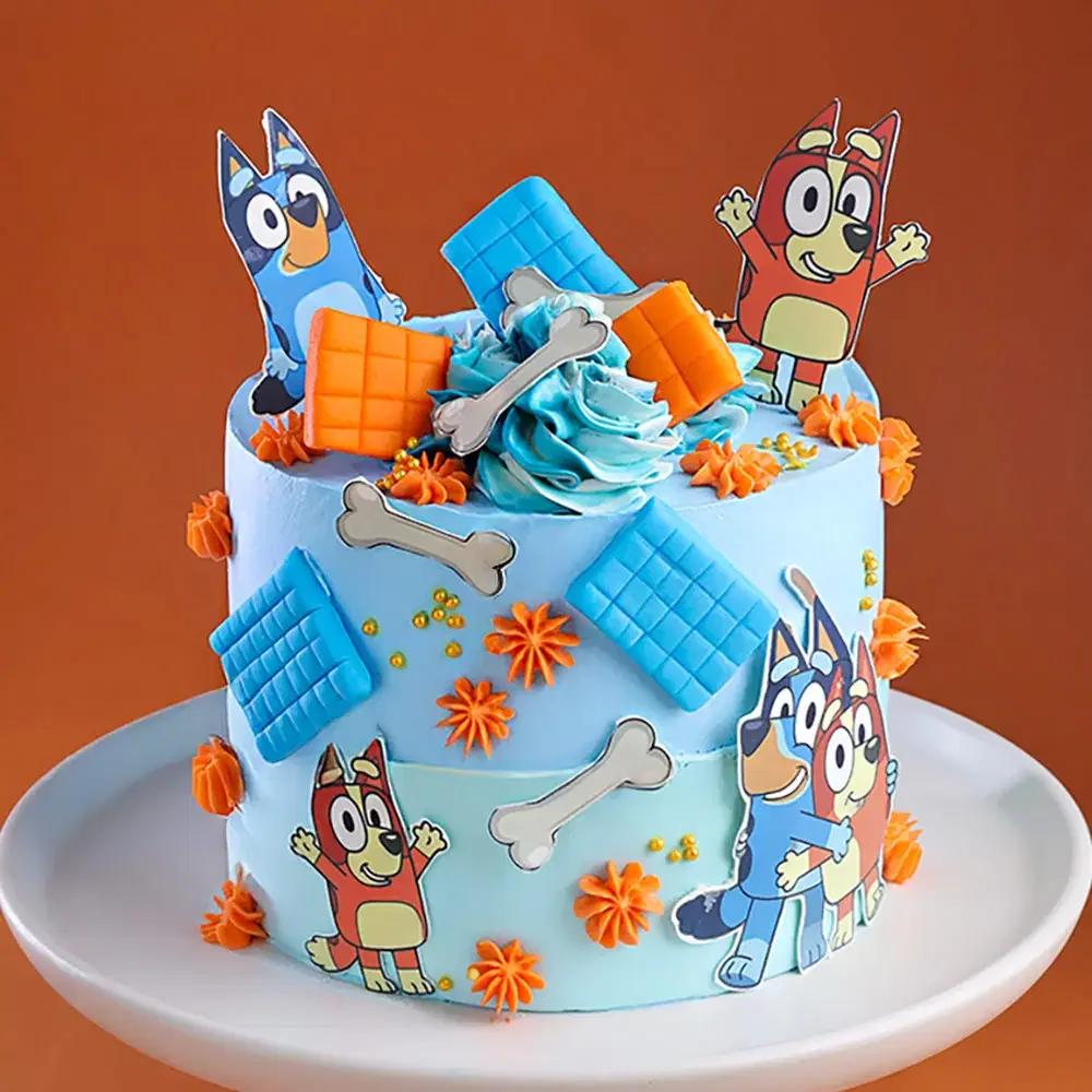 Bluey and Bingo themed light blue birthday cake with orange icing rosettes, fondant bones, and blue chocolate bar decorations.