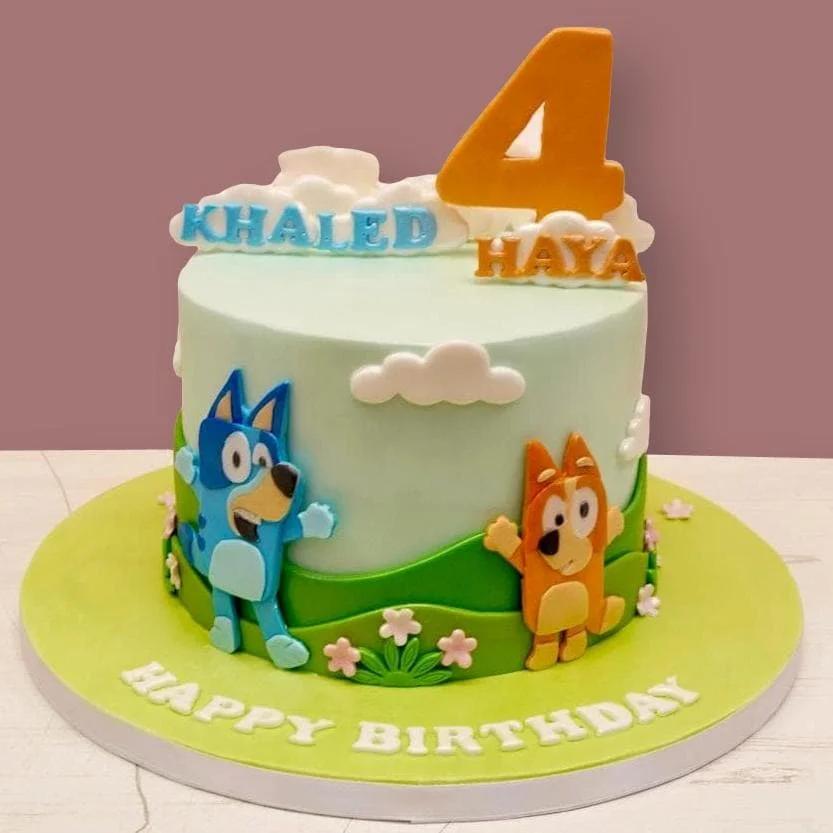 Bluey and Bingo themed birthday cake with green hills, white clouds, and a large orange number four topper.