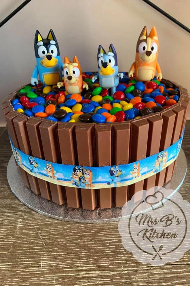 Bluey themed KitKat cake with M&Ms and plastic character figurines on top