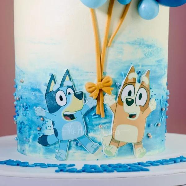 Bluey and Bingo themed birthday cake with blue watercolor icing, sprinkles, and fondant balloon strings.