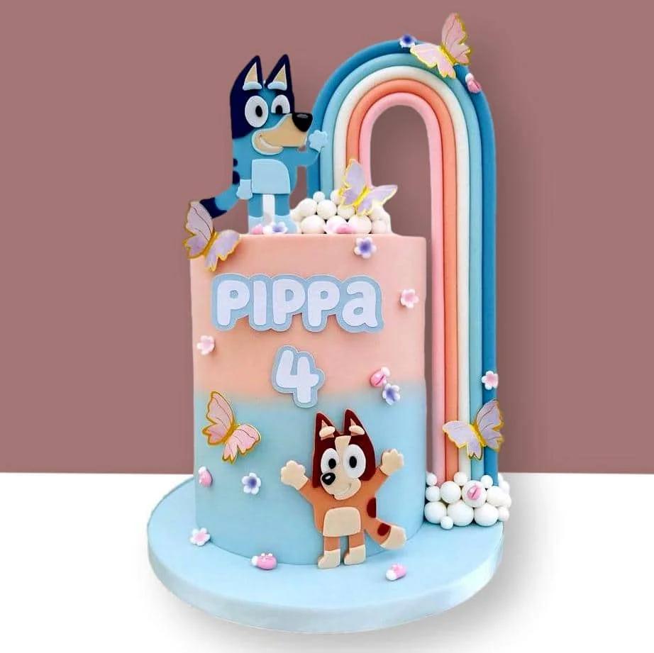 Bluey and Bingo themed birthday cake with a large rainbow and butterfly accents in pink and blue gradient fondant.