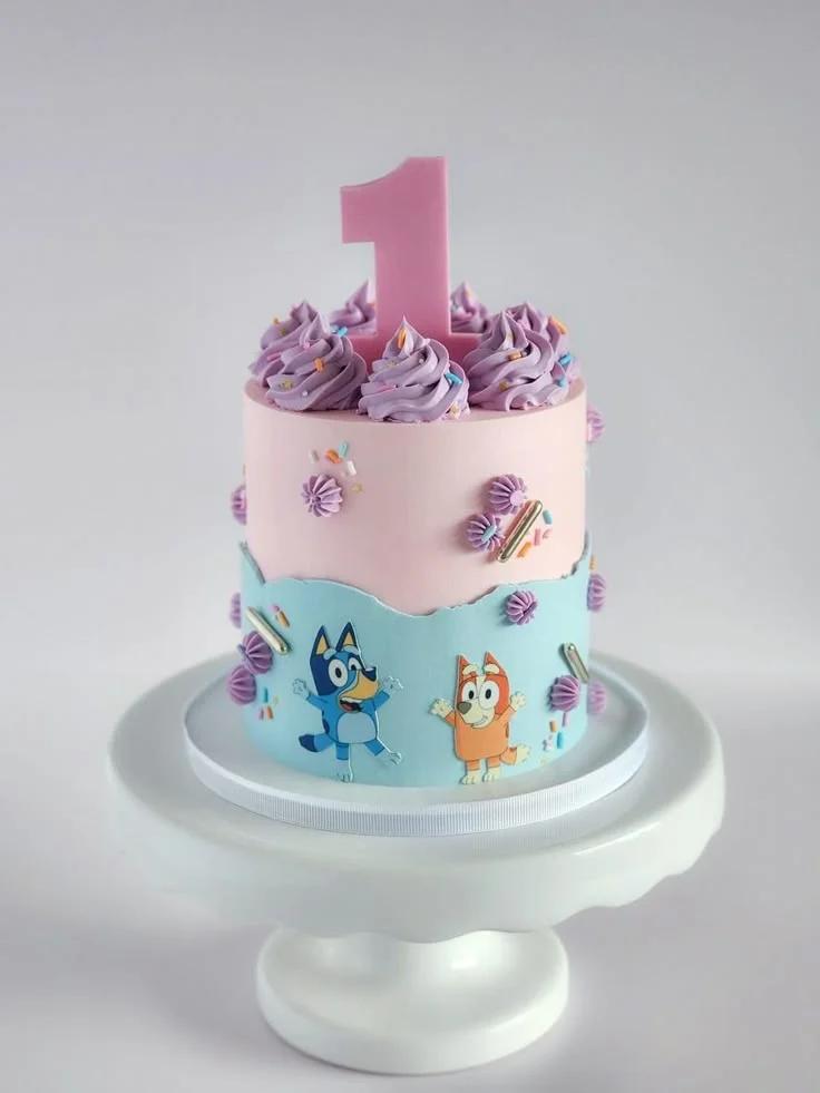 Bluey and Bingo themed pink and light blue birthday cake with a large pink number one topper and purple icing swirls.