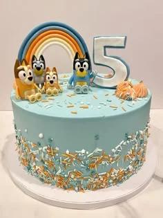 Light blue Bluey themed birthday cake with a fondant rainbow, number 5 topper, and Bluey character figurines.