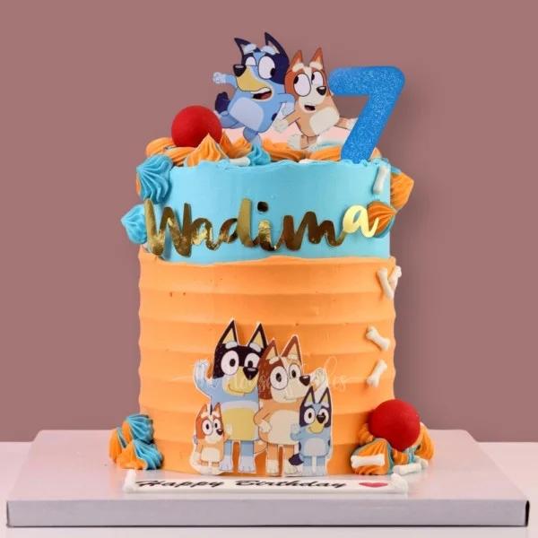 Blue and orange Bluey themed birthday cake with character printouts, icing rosettes, and a gold name topper.