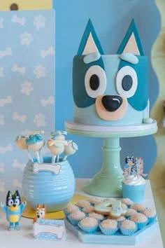 Bluey character themed light blue fondant cake with 3D fondant ears and facial features on a mint green cake stand.