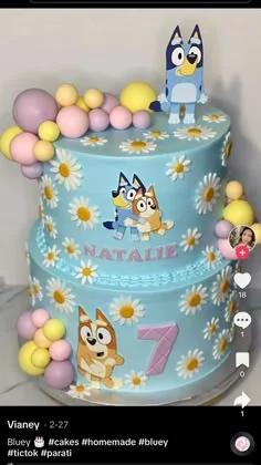 Bluey themed two-tier light blue cake with daisy flowers, fondant balls, and character printouts for a 7th birthday.