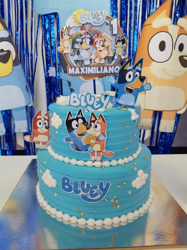 Bluey themed 2-tier light blue cake with character printouts, white icing clouds, and gold stars.