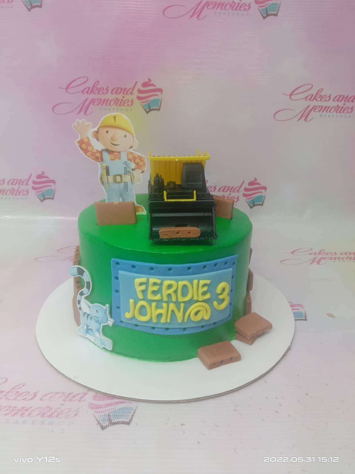 Green Bob the Builder themed birthday cake with a toy construction truck and fondant brick decorations.