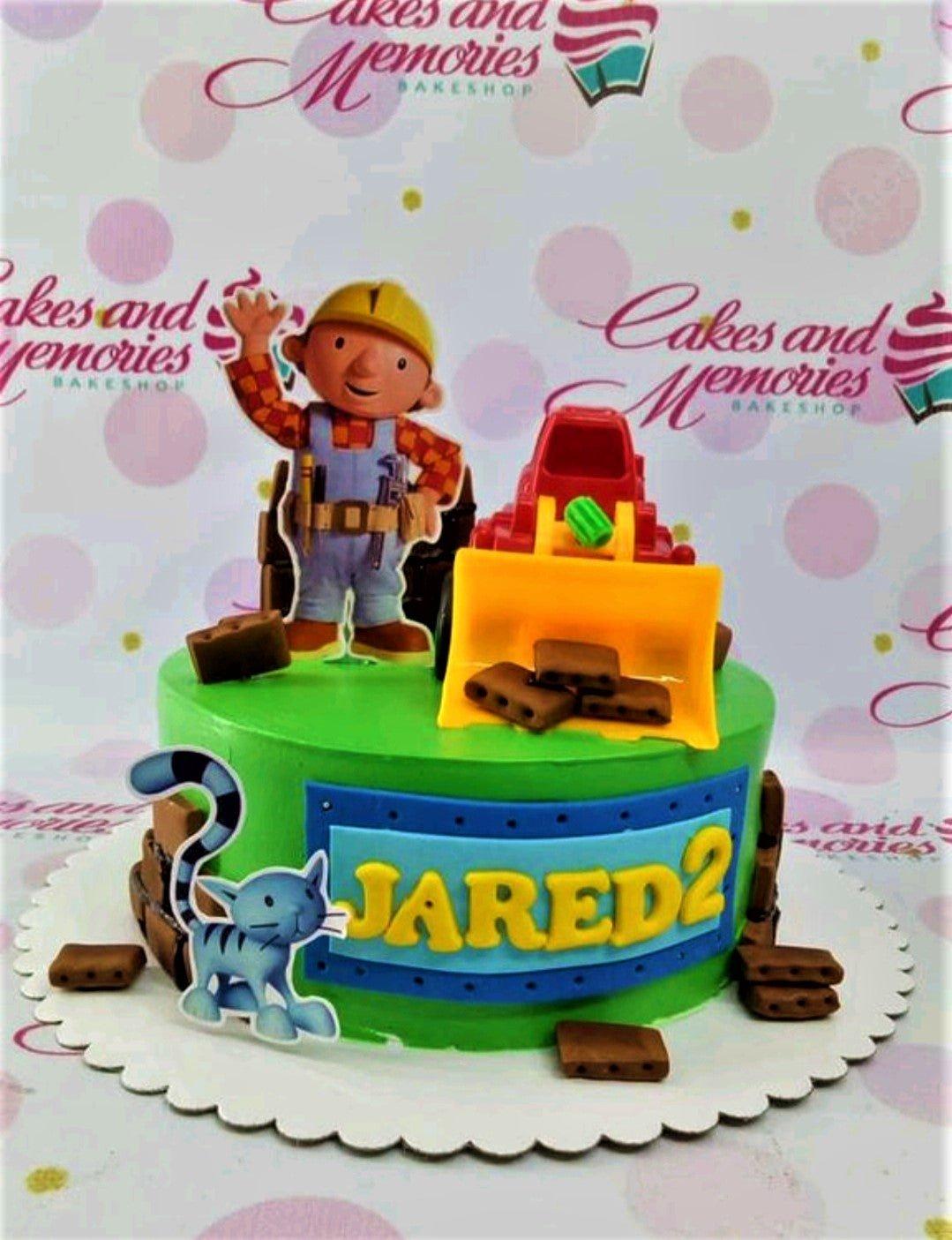 Green Bob the Builder themed birthday cake with a red toy excavator, character printouts, and fondant bricks for Jared's 2nd birthday.