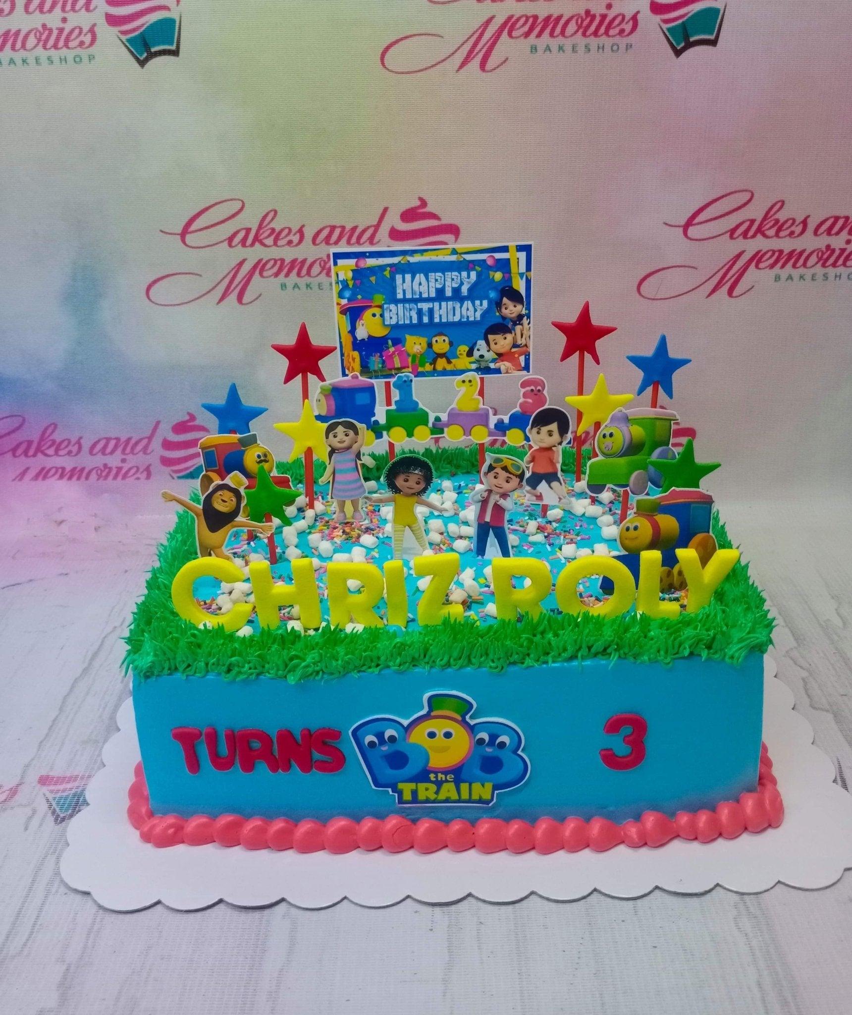 Blue square Bob the Train birthday cake with green grass icing, character printouts, and colorful stars.
