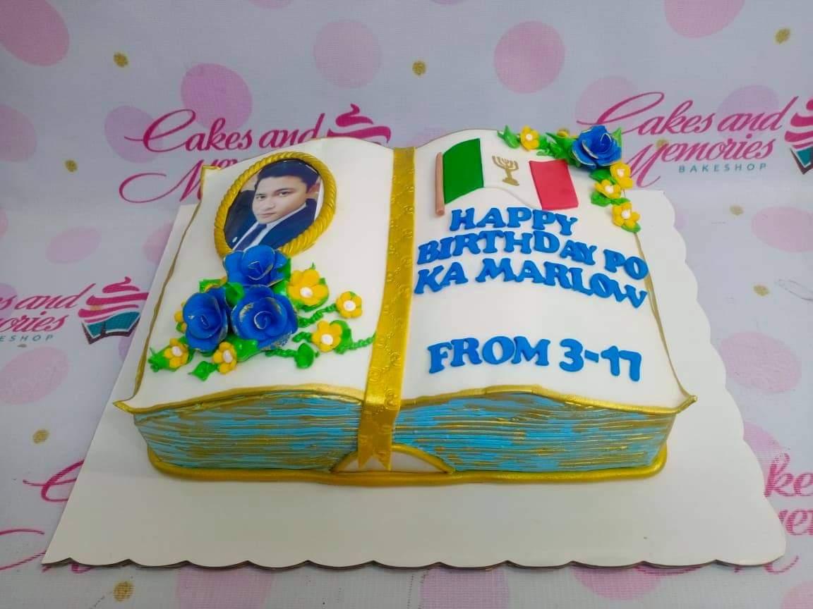 Open book cake with a photo printout, blue and yellow icing roses, and a message for Ka Marlow.