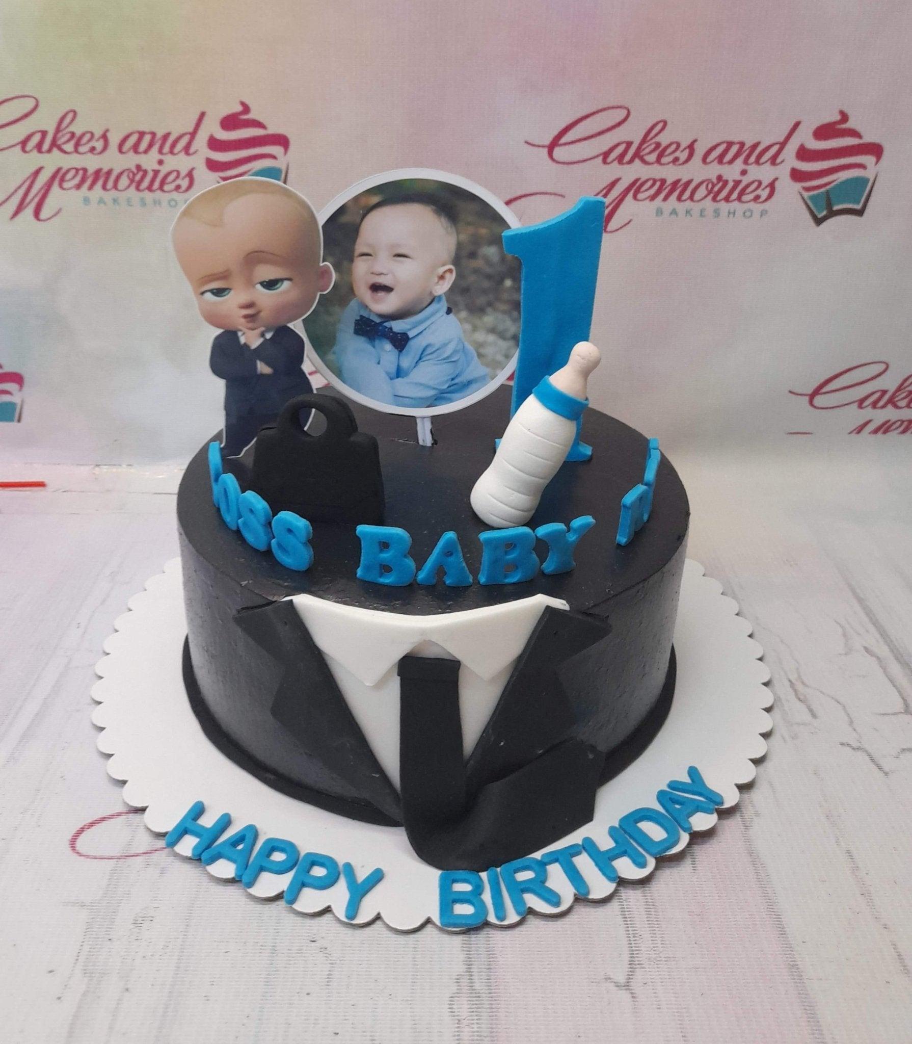 Boss Baby themed black tuxedo cake with a photo topper and blue accents for a first birthday celebration.