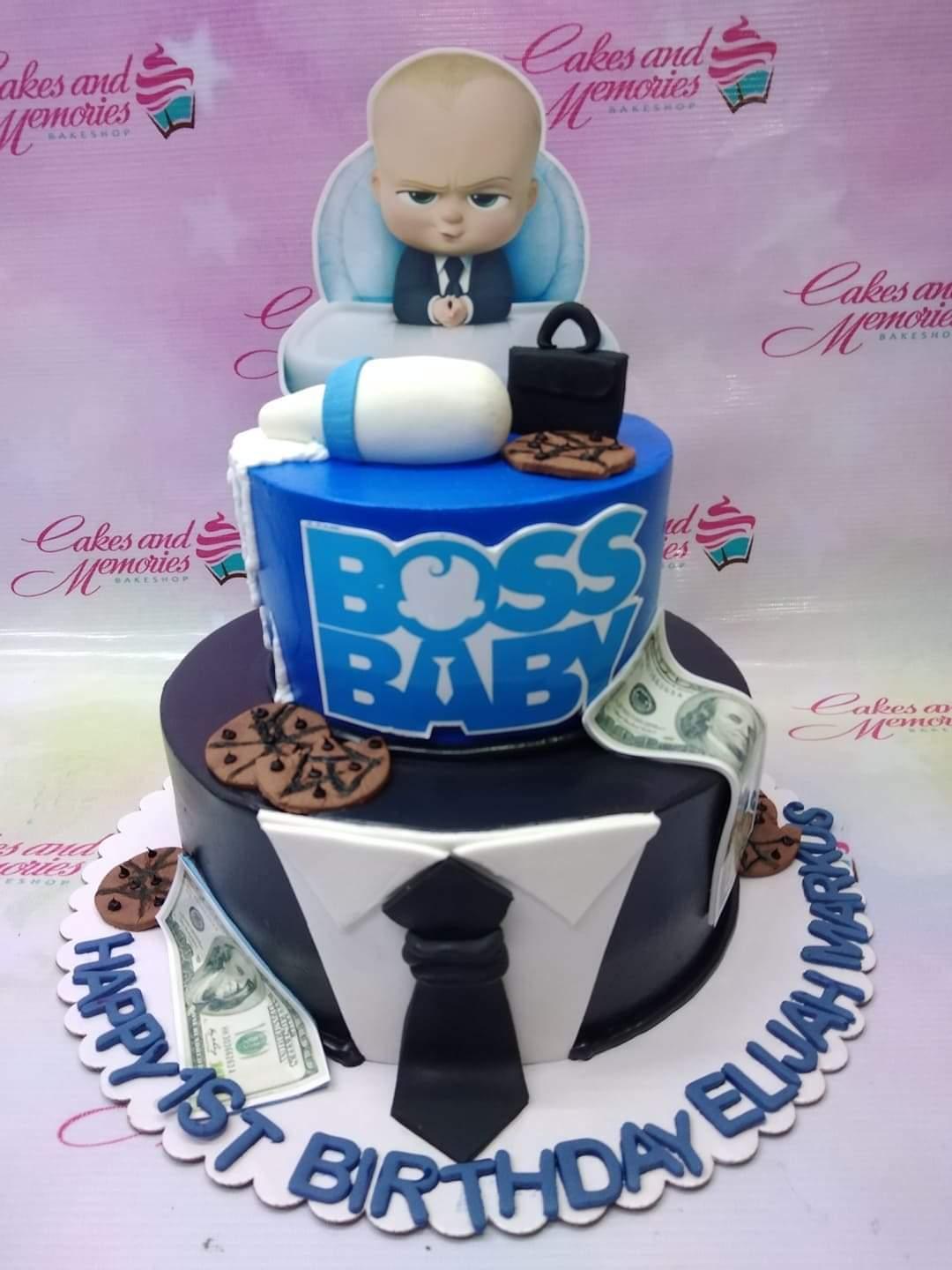 Two-tier Boss Baby themed birthday cake in blue and black with fondant tuxedo details, money, and cookies.