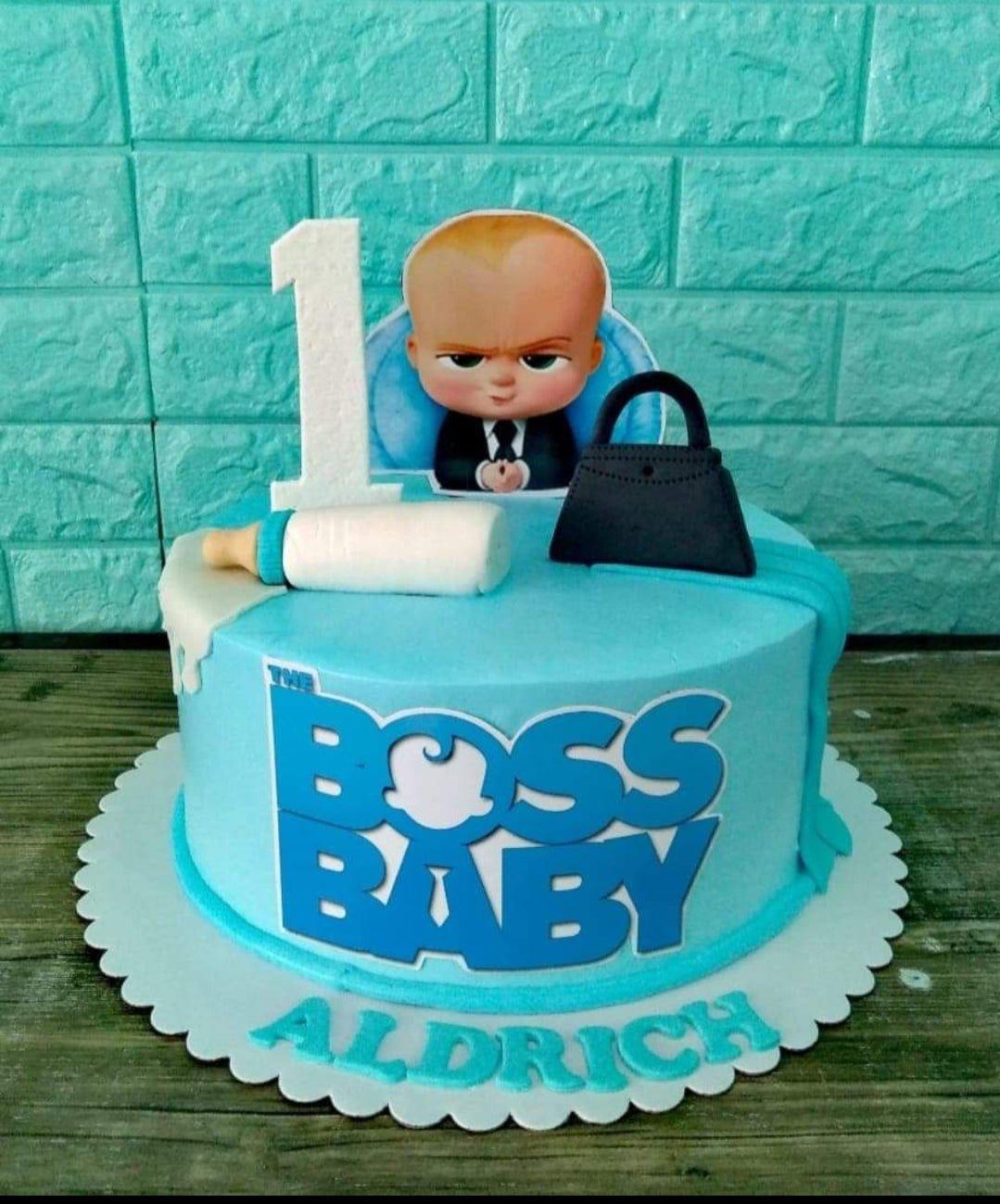 Light blue Boss Baby themed birthday cake with a baby bottle, briefcase, and character printout for Aldrich's 1st birthday.