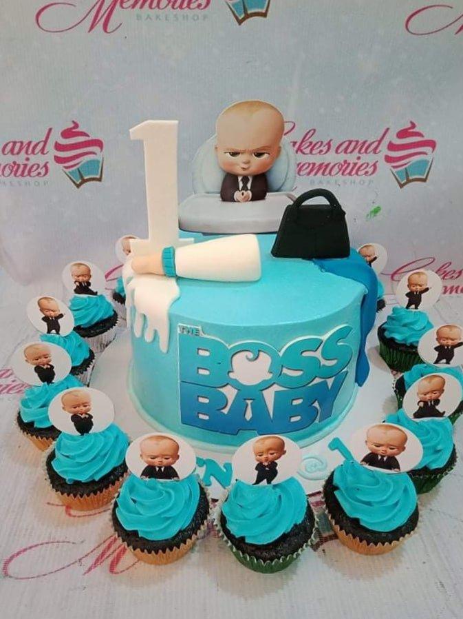 Light blue Boss Baby themed birthday cake with a 3D baby figure, milk bottle, and briefcase toppers surrounded by matching cupcakes.