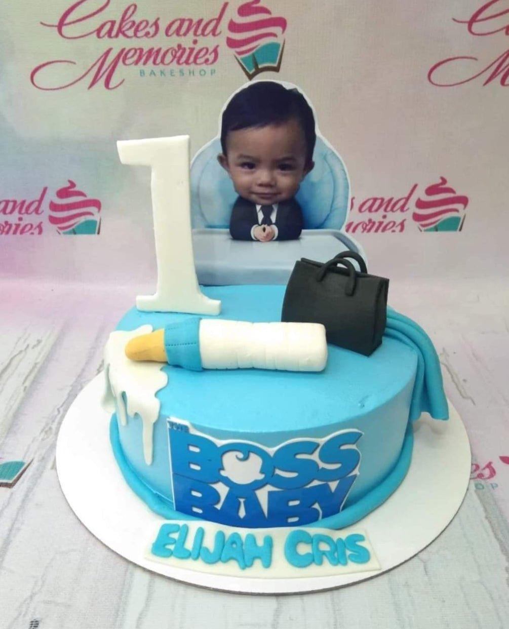 Light blue Boss Baby themed birthday cake with a photo printout of a baby, a fondant milk bottle, and a black briefcase topper.