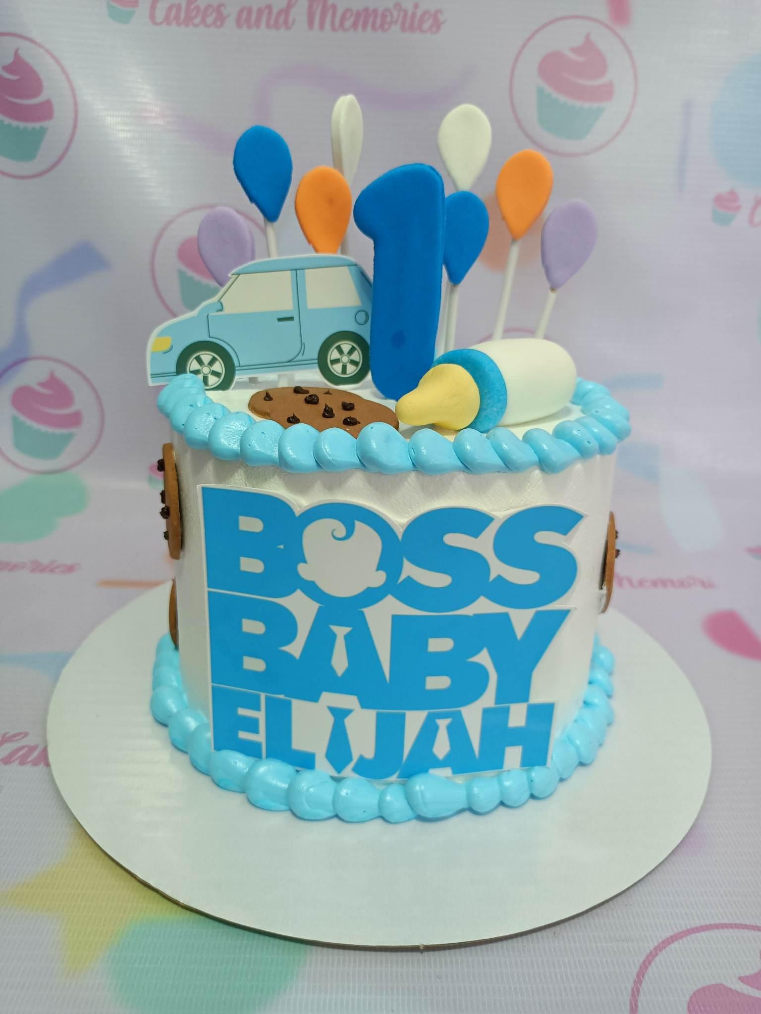 Boss Baby Elijah themed white cake with light blue icing borders, a blue number one topper, a car printout, and a baby bottle fondant figure.