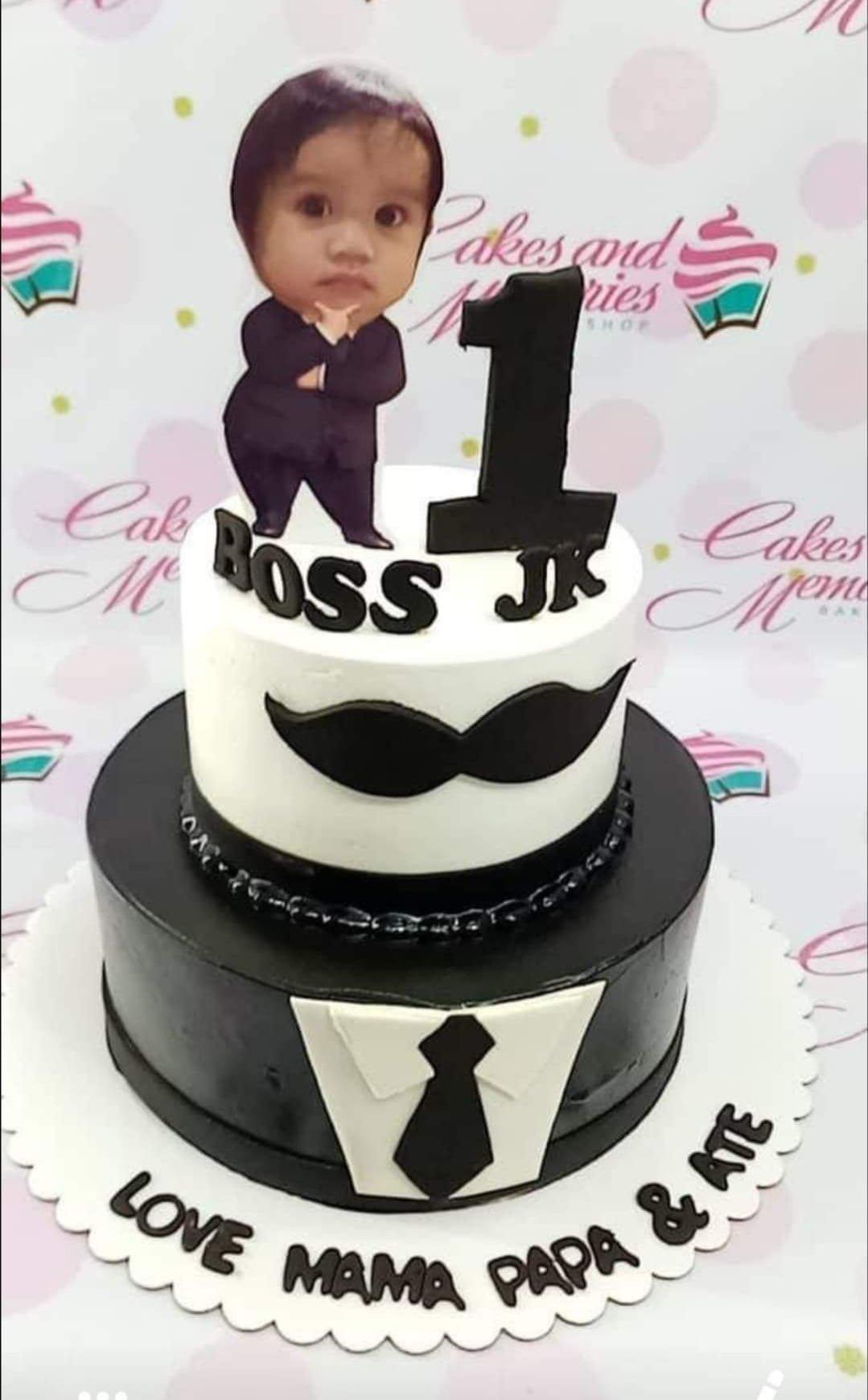 Two-tier Boss Baby themed birthday cake with a black tuxedo bottom tier and white top tier featuring a mustache and character printout.